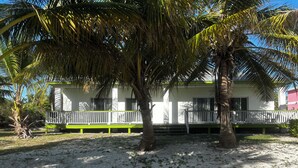 A two-story building with a white exterior and green accents, featuring a balcony with a white railing. - Beachfront Paradise in Rolleville Steps to Sand, Pig Beach & Coco Plum (Exuma)