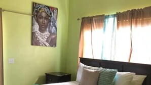 A bedroom with a bed, a nightstand, a painting on the wall, and a window with curtains. - Beachfront Paradise in Rolleville Steps to Sand, Pig Beach & Coco Plum (Exuma)