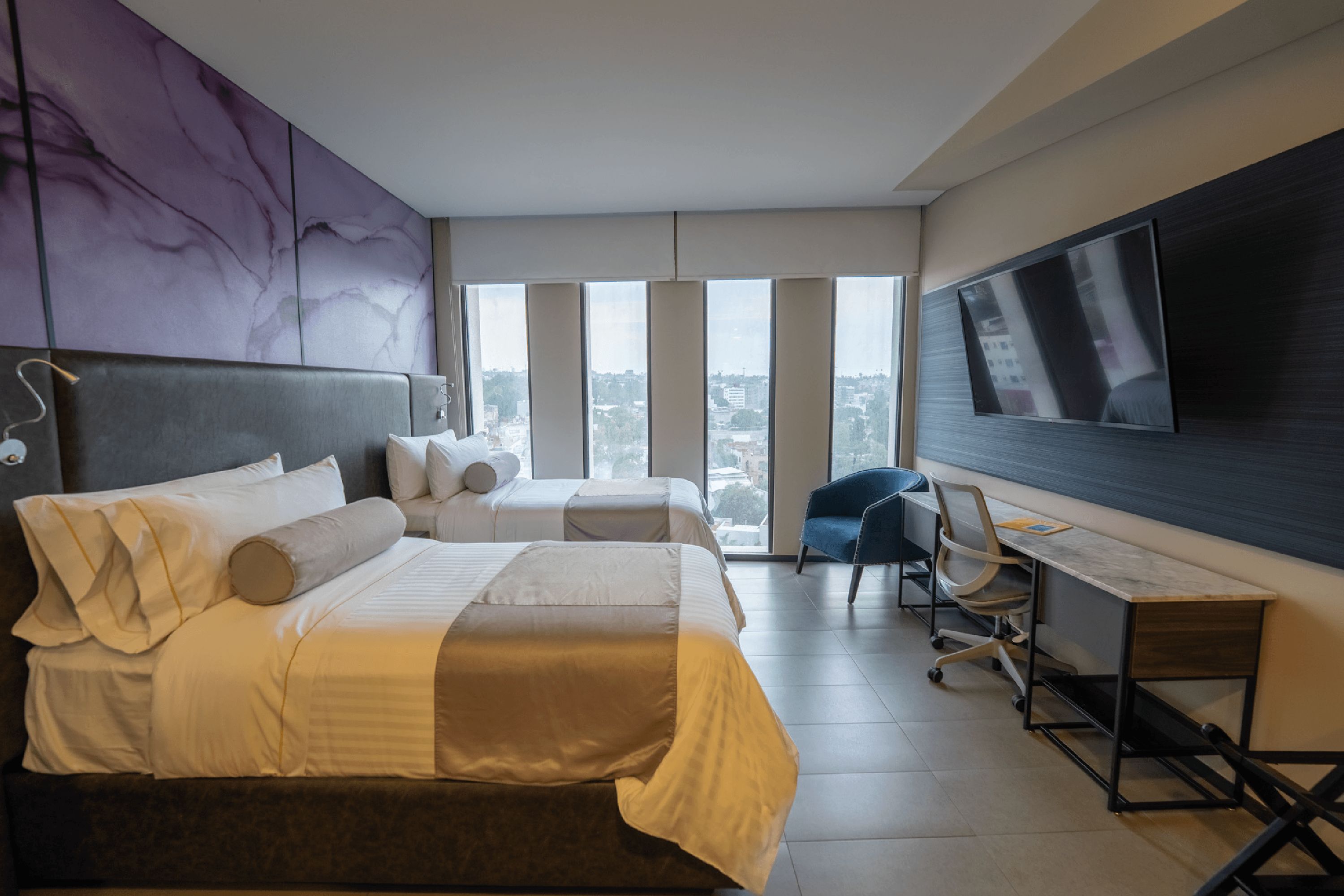 Ein Hotelzimmer mit einem großen Bett, einem Schreibtisch, einem Sessel und einem an der Wand befestigten Fernseher.
