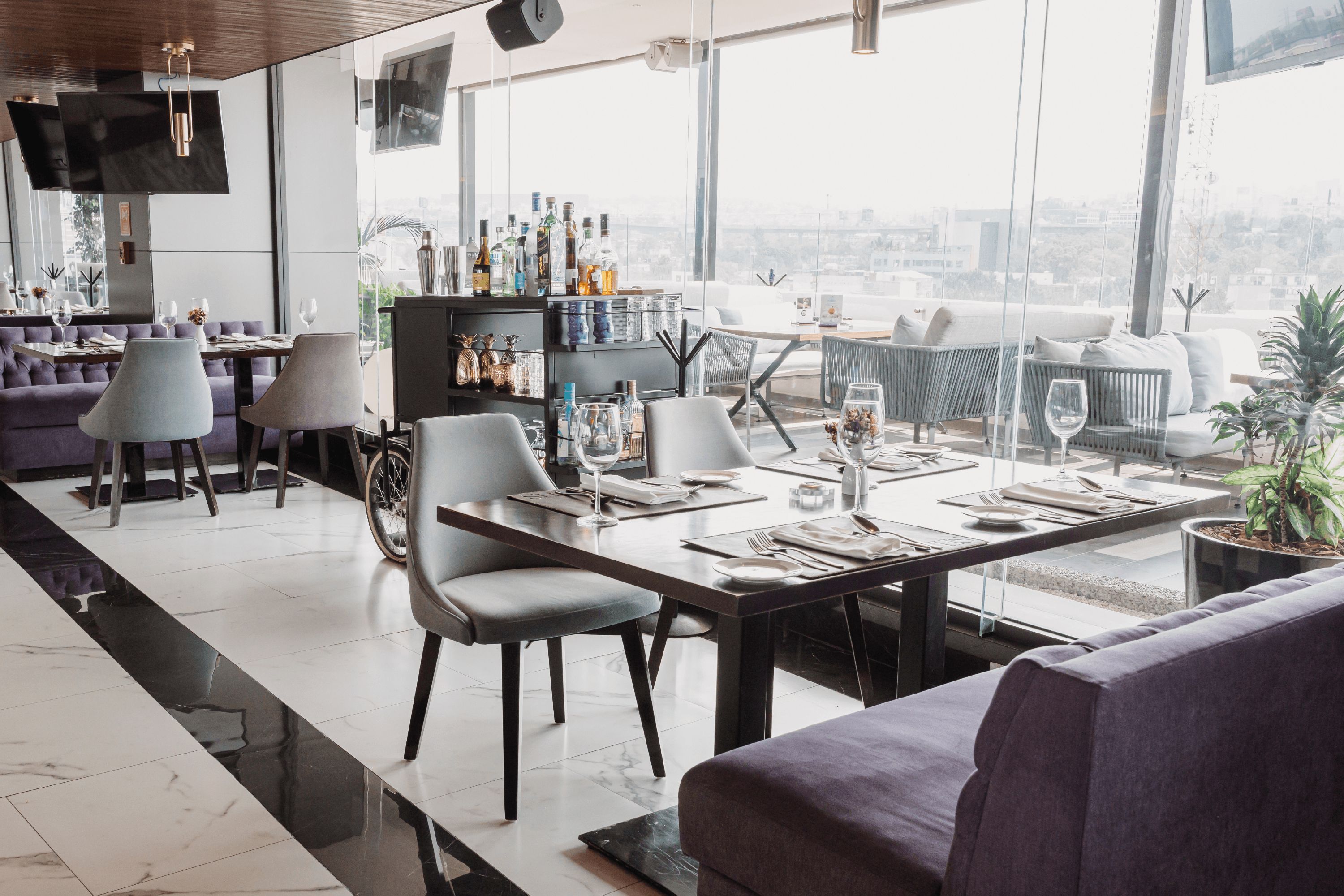 Un espace repas moderne avec une longue table, des chaises et un canapé. On y trouve également un coin bar avec des bouteilles et des verres.
