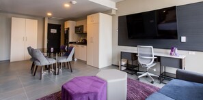 Un salon moderne comprenant un coin repas, une cuisine et un téléviseur fixé au mur.