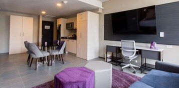 Una sala de estar moderna con comedor, cocina y televisor montado en la pared.