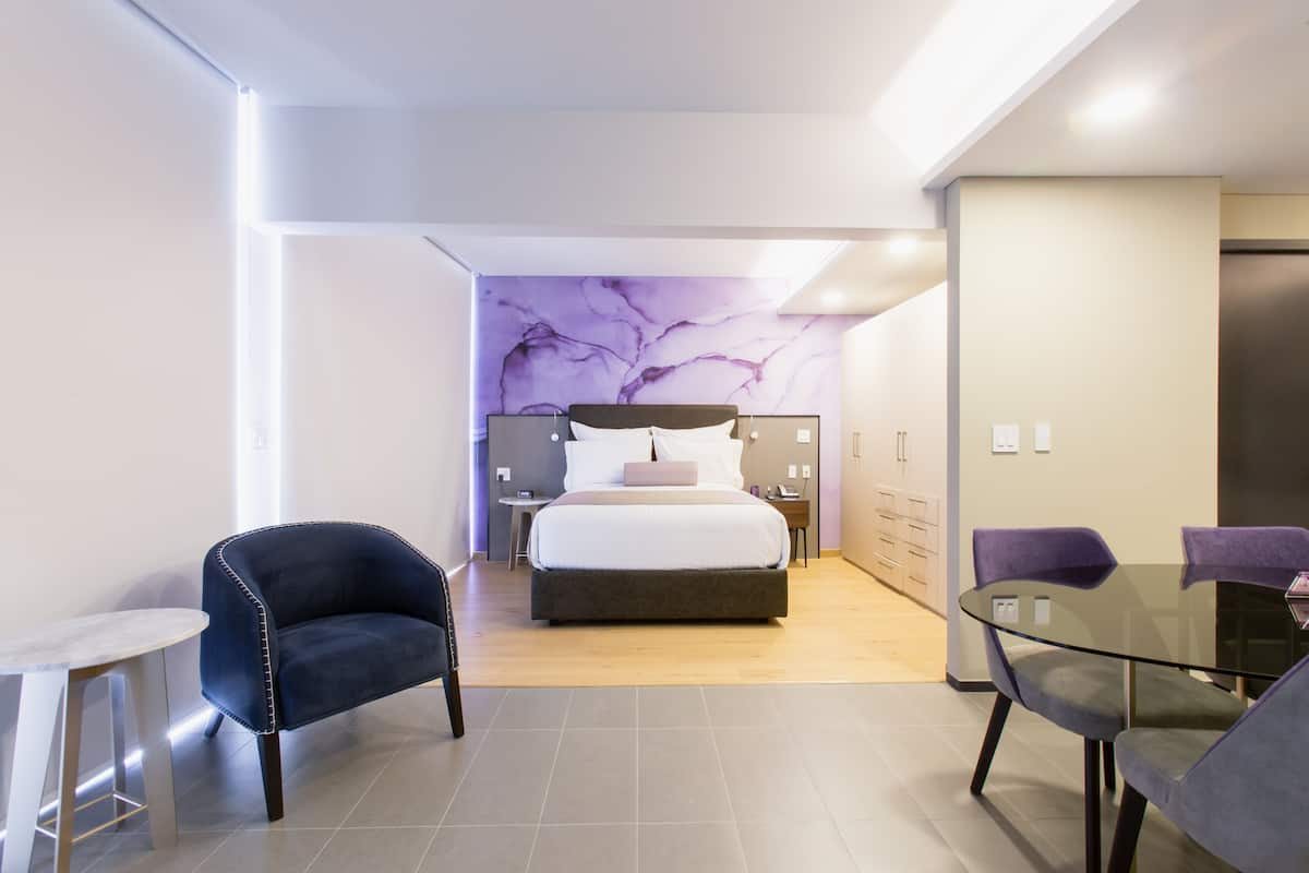 Une chambre d’hôtel moderne, équipée d’un lit, d’une table en verre et de deux chaises.