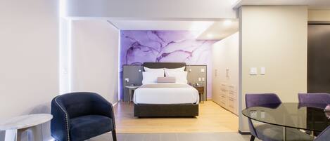 A modern hotel room with a bed, a glass table, and two chairs.