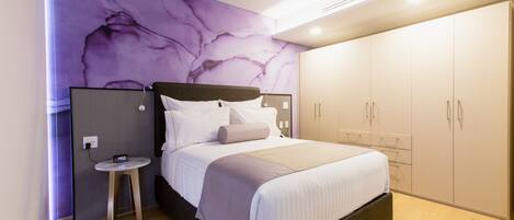 A modern bedroom with a large bed, a nightstand, a wardrobe, and a marble-patterned wall.
