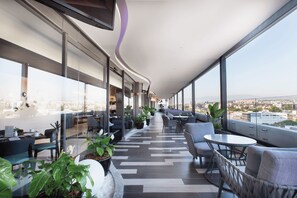 A modern lounge area with seating and tables, large windows offering a city view, and a curved ceiling design. - HS HOTSSON Long Stay CDMX Condesa Sur (Mexico City)