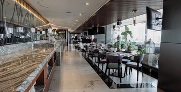 Interior moderno de restaurante con mostradores de mármol, mesas, sillas y un gran ventanal con vistas a la ciudad.