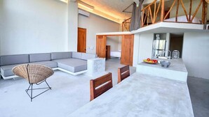 Een moderne woonkamer met een hoekbank, een rieten stoel en een eethoek met een tafel en stoelen.