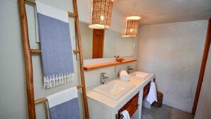Een badkamer met twee wastafels, een houten ladder, een spiegel en gevlochten lampen.