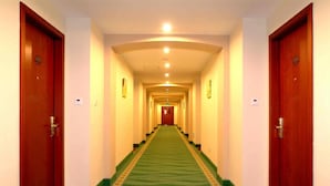 A hotel hallway with a green carpet, wooden doors, and a light-colored ceiling. - Greentree Inn Beijing Shunyi District New International Exhibition Express Hotel (Beijing)