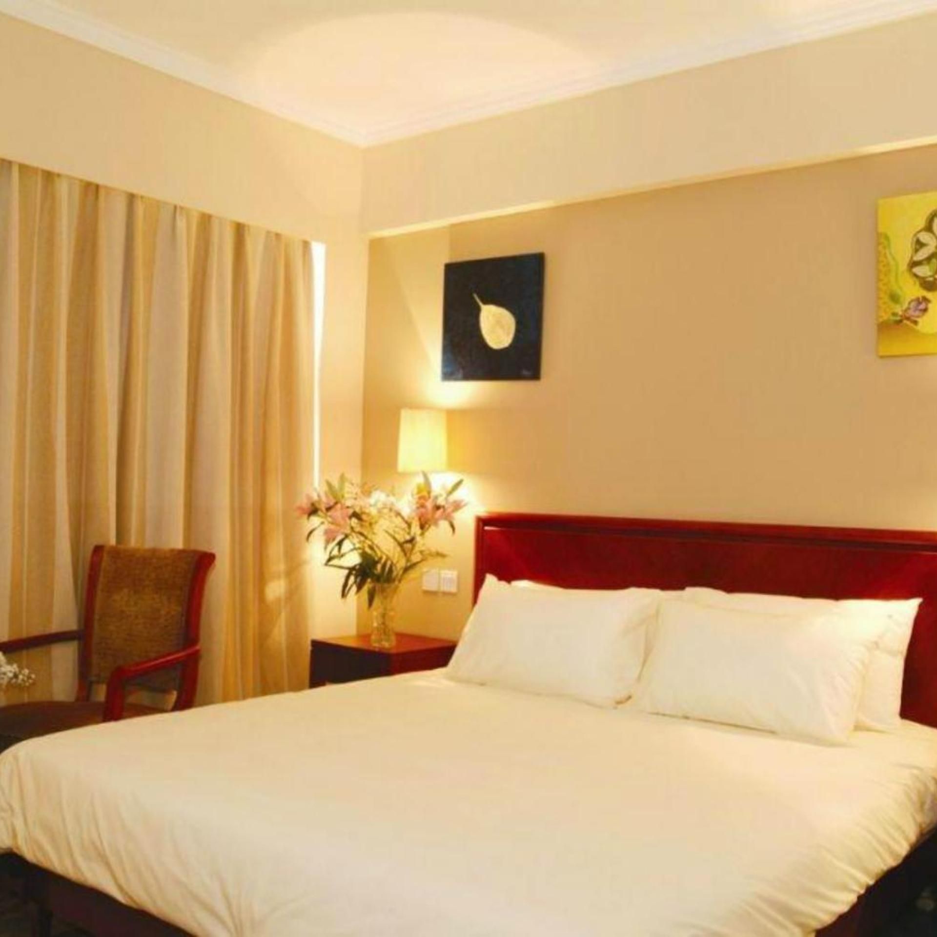 A hotel room with a bed, a chair, a nightstand with a lamp, and a wall with a framed picture.