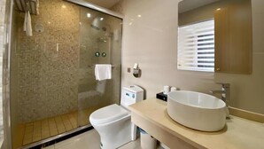 Une salle de bain moderne avec une douche à parois de verre, des toilettes, un grand lavabo et un miroir.
