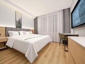 A modern hotel room with a bed, bedside table, desk, and a television mounted on the wall.