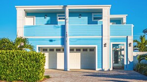 Een modern herenhuis met twee verdiepingen, een blauwe gevel en witte details, met twee garages en een verzorgde voortuin.