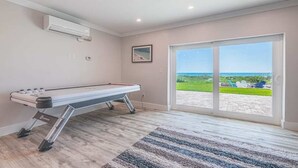 Een kamer met een pooltafel, een grote schuifpui naar een terras en uitzicht op de oceaan.
