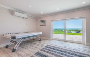 A room with a pool table, a large sliding glass door to a patio, and a view of the ocean.