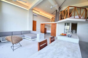 Un espacio moderno de estar con sofá, una silla de mimbre, una mesa de comedor con sillas y una cocina con lavamanos y frutero.