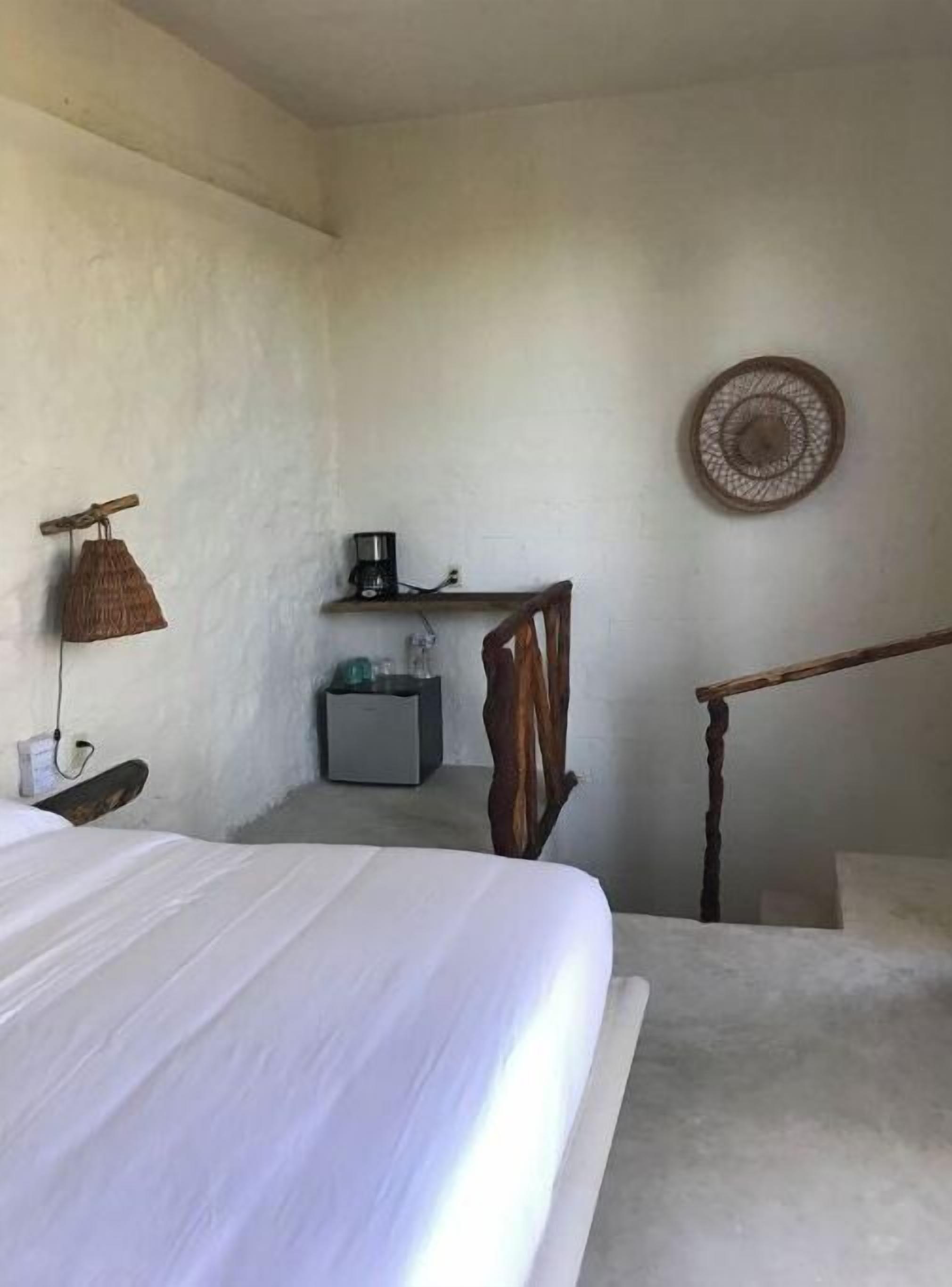 A bedroom with a bed, a nightstand, a coffee maker, a small cabinet, and a wooden chair.