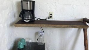 Uma cozinha compacta com cafeteira em uma prateleira, uma pequena geladeira e um recipiente de vidro na bancada.