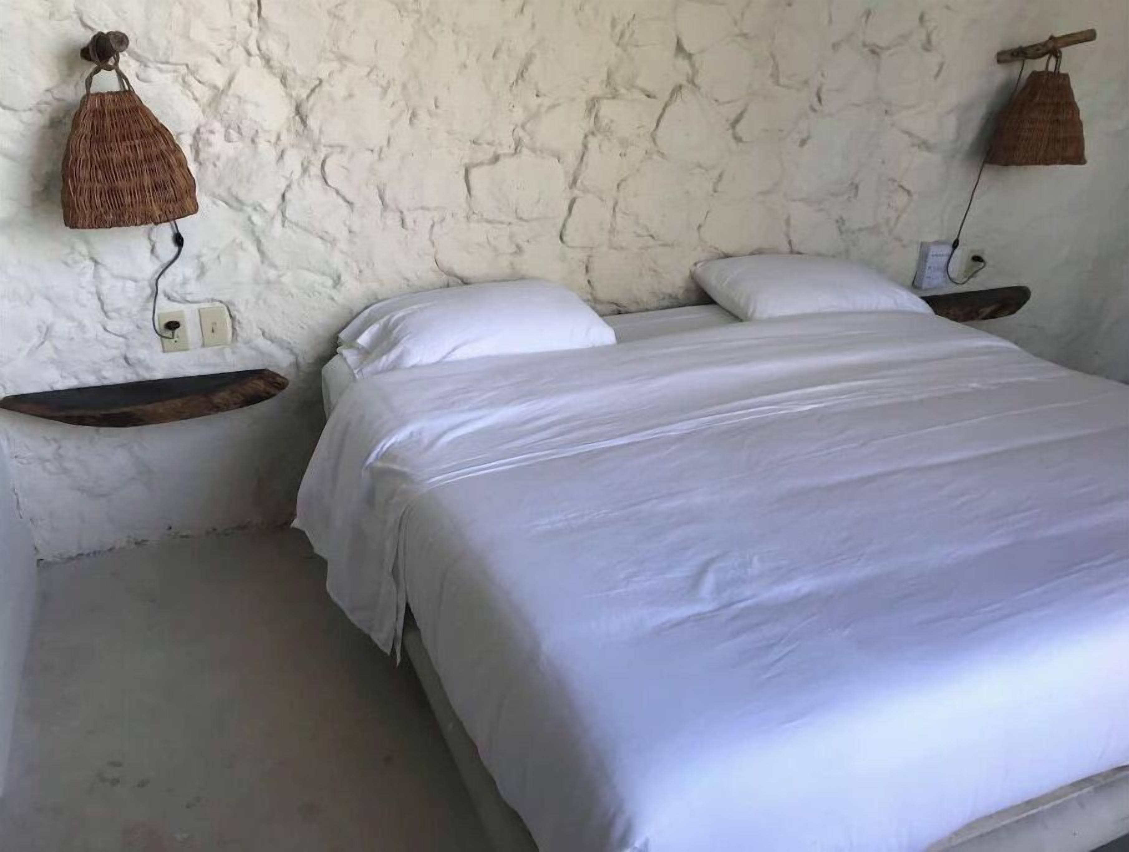Un letto con biancheria da letto bianca in una stanza con parete bianca strutturata.