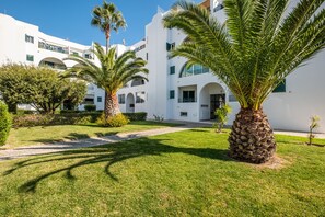 A white building with multiple balconies, palm trees, and a clear sky.
