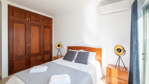 Ein Schlafzimmer mit einem Bett, einem Holzschrank, Nachttischen und einer Klimaanlage.