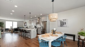 A modern kitchen with white cabinets, stainless steel appliances, and a dining area with blue chairs and a white table. - Ultimate Downtown Charlotte Oasis, 10 Guests (Charlotte)
