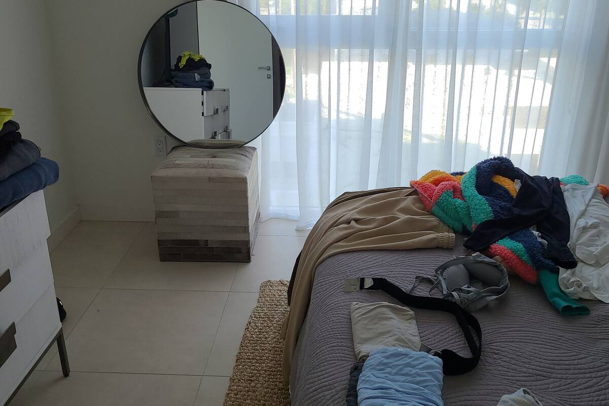 A bedroom with a bed, a bedside table, a mirror, and a window with curtains.