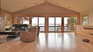 Ein geräumiges Wohnzimmer mit hohen Decken, großen Fenstern und Blick auf einen Steg.