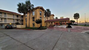 A multi-story hotel with a red-tiled roof, a covered entrance, and a parking area with a few cars.