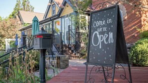 A wooden deck with a sign reading "Come in We're Open" and a building with a green awning in the background.