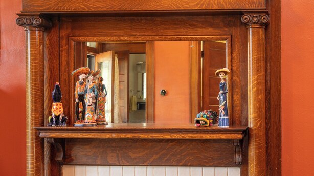 A fireplace with a mirror above it, flanked by wooden mantels and a vase of flowers.