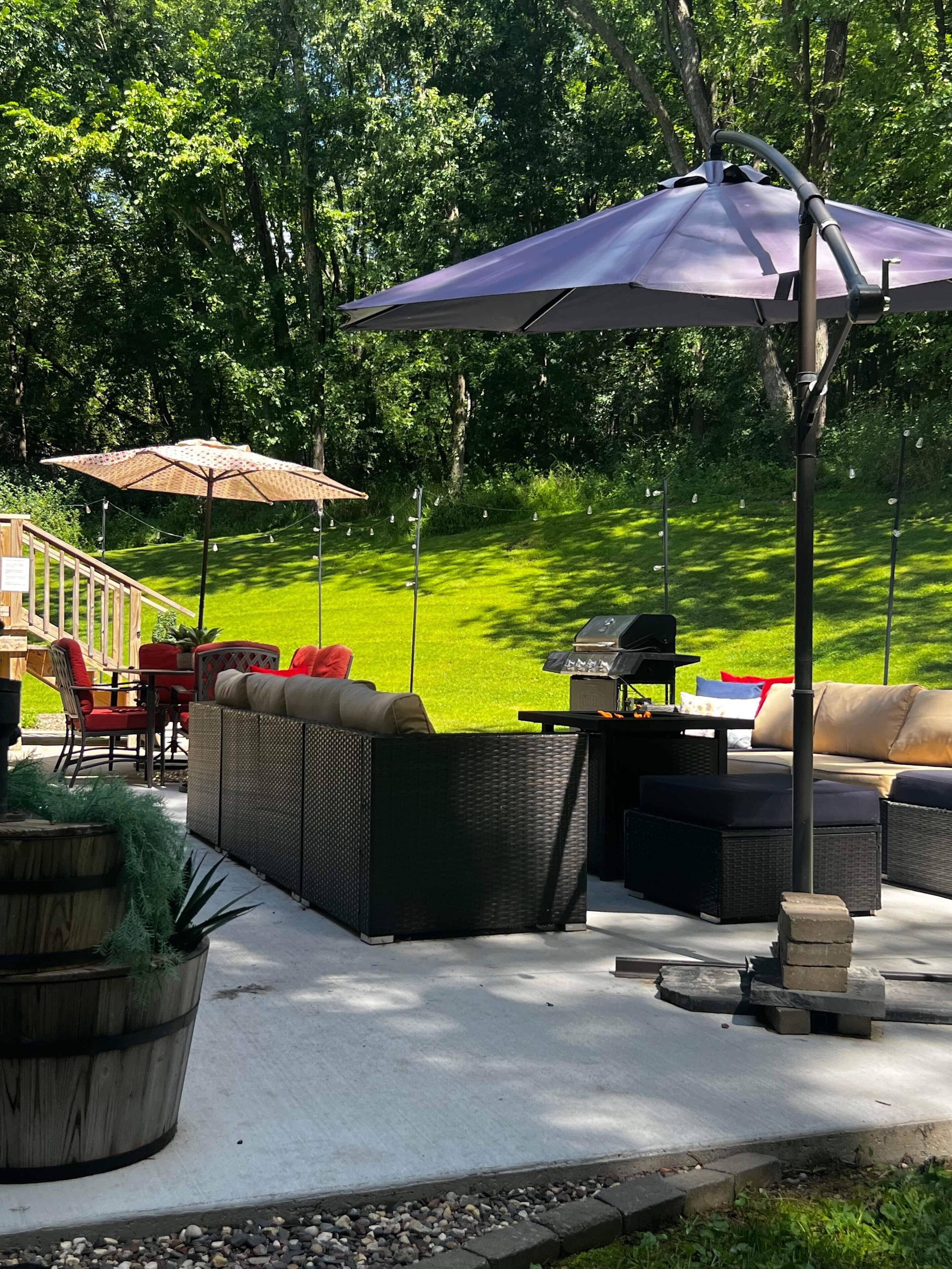 An outdoor patio with wicker furniture, a barbecue grill, and umbrellas.