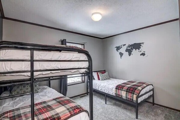 A dormitory room with bunk beds and a single bed, a world map on the wall, and a window.