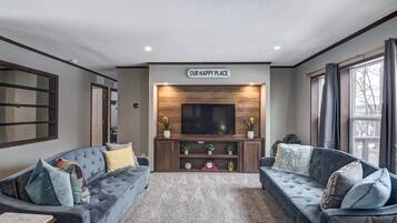 A living room with two sofas, a TV, and a 'OUR HAPPY PLACE' sign.