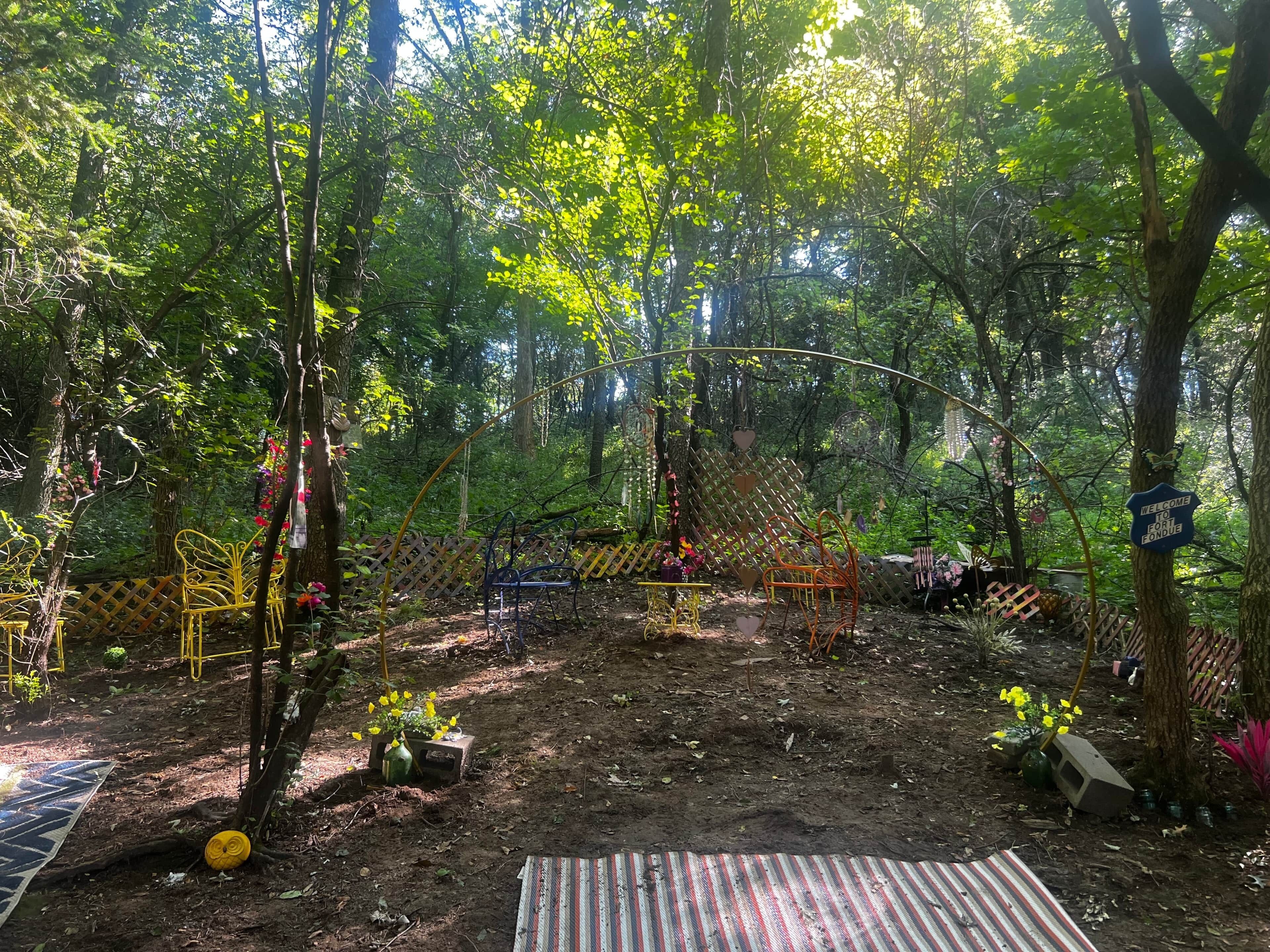 A forested area with a wooden fence, metal chairs, and a welcome sign.