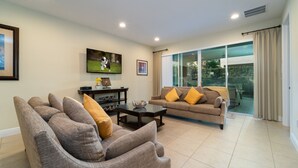 A living room with a sofa, a coffee table, and a TV mounted on the wall. - Amazing Home With Spa & Games Room In Gated Resort Close to WDW (Kissimmee)