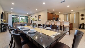 A spacious dining area with a long table, multiple chairs, and a kitchen in the background. - Amazing Home With Spa & Games Room In Gated Resort Close to WDW (Kissimmee)