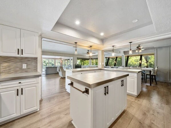 Una cocina amplia con una isla grande, armarios blancos e iluminación colgante.