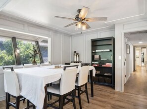 A dining area with a table set for four, a ceiling fan, and a bookshelf in the background.