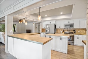 Una cocina moderna con armarios blancos, una isla central, electrodomésticos de acero inoxidable e iluminación colgante.