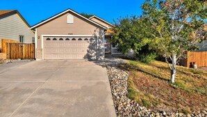 A residential garage with a number 7542 on the door, a concrete driveway, and a landscaped area with a tree and a wooden fence. - 4 BED/2 BATH; Sleeps 10! CO Springs- fenced yard, pets w/fee, Great for Families (Colorado Springs)