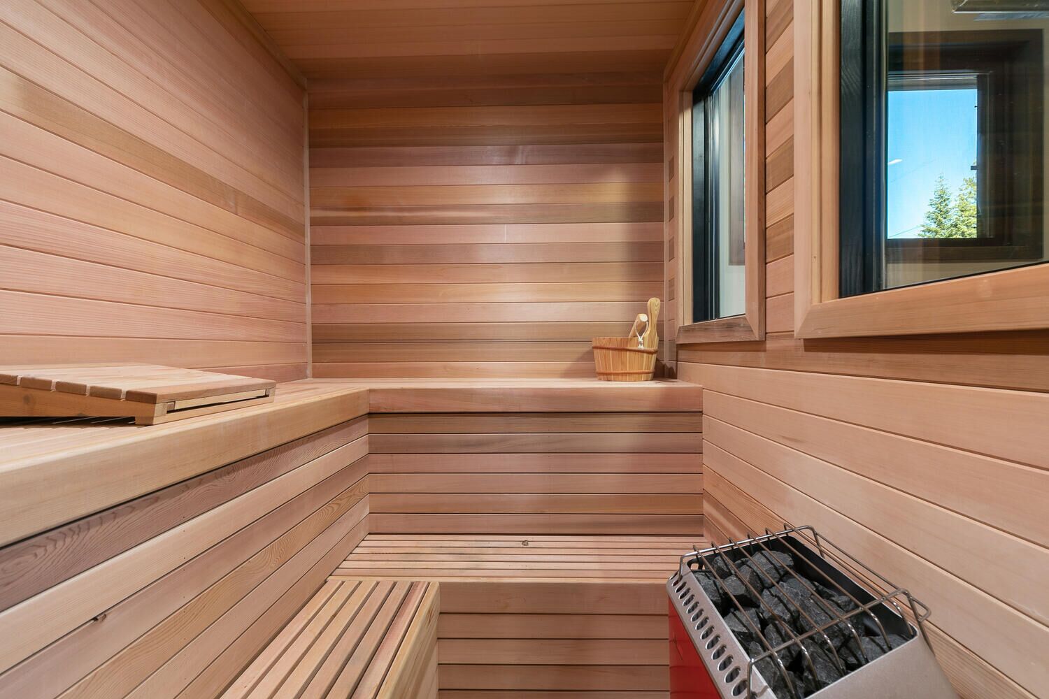 Un sauna avec des murs et des bancs en bois, une fenêtre et un panier contenant divers objets.