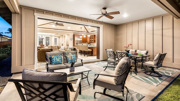Un espace patio aménagé avec du mobilier d’extérieur, un ventilateur de plafond et une vue sur l’intérieur de la maison.