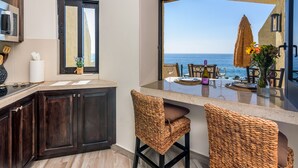 A kitchen with dark wood cabinets, a microwave, and a large window overlooking the sea.