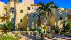 A courtyard with a palm tree, a trash bin, and a sign with a name.