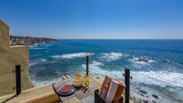 A seaside terrace with a table set for dining, overlooking the ocean.