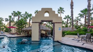 A swimming pool with a thatched-roof archway, palm trees, and outdoor seating.