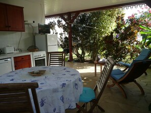 A kitchen with a table and chairs, a refrigerator, and a television. - Bungalow du Voyageur (LE MARIN)
