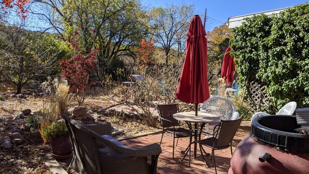An outdoor patio with wicker furniture, red umbrellas, and a brick floor. - Studio apartment 15 minute walk to the plaza (Santa Fe)